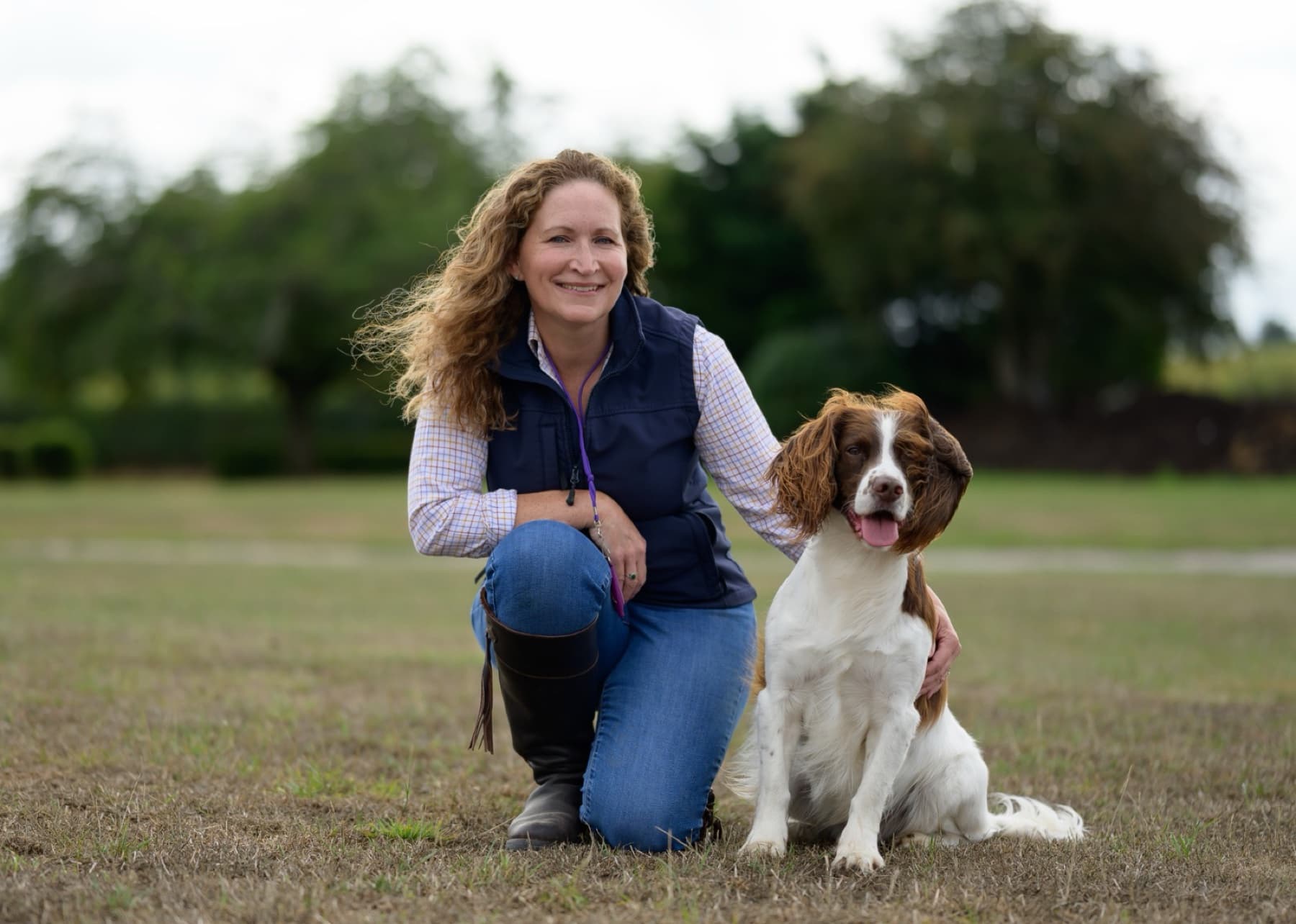 Liz Huntbach kneeling on grass beside her springer spaniel